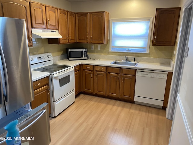 kitchen with decorative backsplash, a sink, appliances with stainless steel finishes, under cabinet range hood, and light wood-type flooring