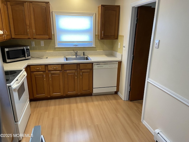 kitchen with a sink, light wood-style floors, light countertops, white appliances, and backsplash