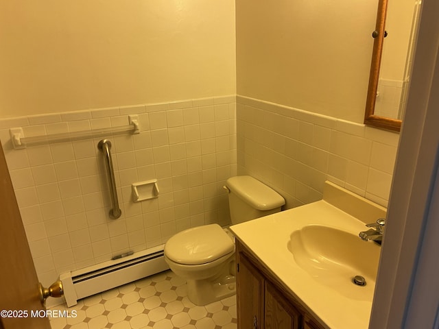 half bathroom with a baseboard heating unit, tile walls, vanity, toilet, and wainscoting