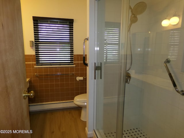 bathroom with a baseboard heating unit, toilet, tile walls, wood finished floors, and a shower stall