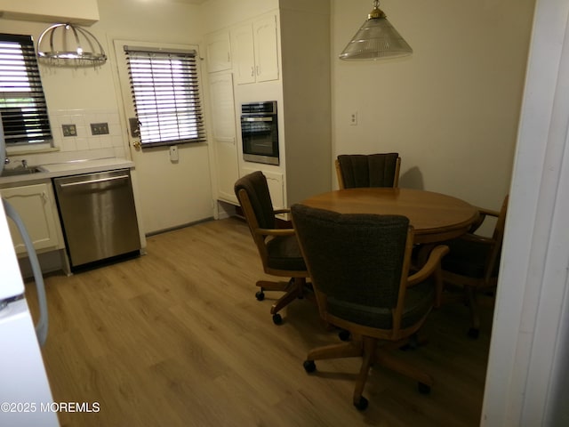 kitchen featuring stainless steel appliances, light wood-type flooring, white cabinetry, light countertops, and hanging light fixtures