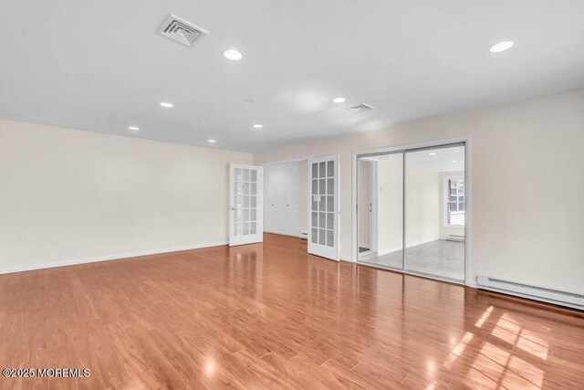 empty room featuring baseboard heating, wood finished floors, visible vents, and recessed lighting