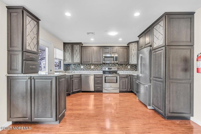 kitchen with a sink, decorative backsplash, stainless steel appliances, light wood-style flooring, and visible vents