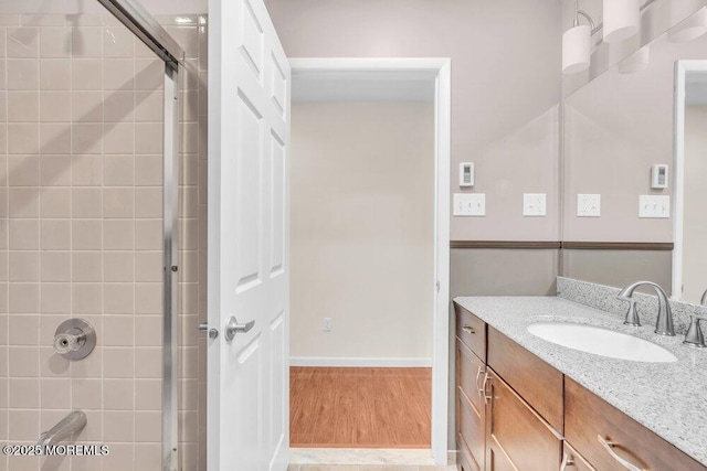 bathroom featuring baseboards, walk in shower, vanity, and wood finished floors