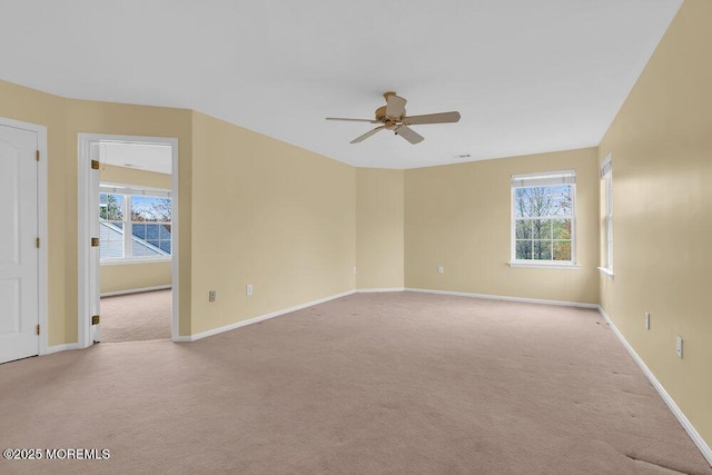 empty room featuring light colored carpet, a ceiling fan, baseboards, and plenty of natural light