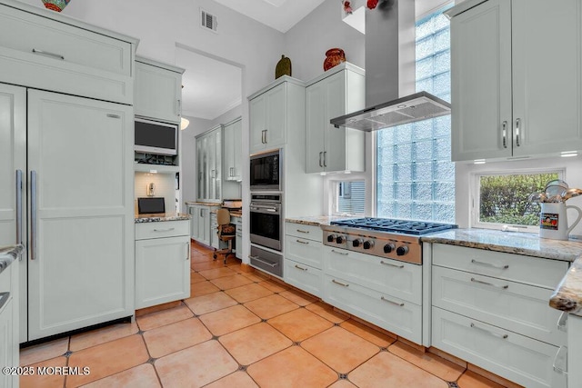 kitchen featuring wall chimney range hood, a healthy amount of sunlight, light stone countertops, light tile patterned floors, and built in appliances