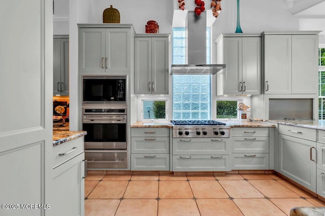 kitchen featuring a warming drawer, appliances with stainless steel finishes, light stone counters, and wall chimney exhaust hood