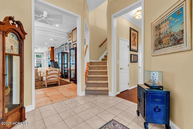 foyer featuring ceiling fan, light tile patterned floors, baseboards, ornamental molding, and stairs