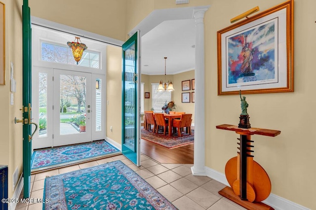 foyer entrance with baseboards, ornate columns, light tile patterned flooring, and a chandelier