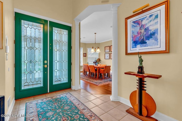 entryway with crown molding, light tile patterned floors, baseboards, a notable chandelier, and ornate columns