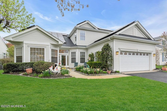 view of front of property with an attached garage, driveway, a front yard, and solar panels