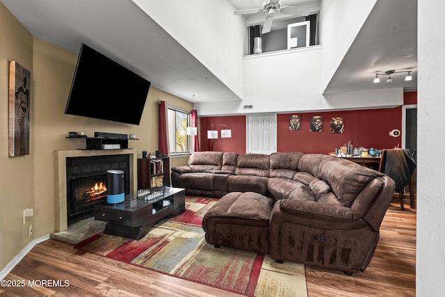 living room featuring a warm lit fireplace, wood finished floors, visible vents, and a ceiling fan