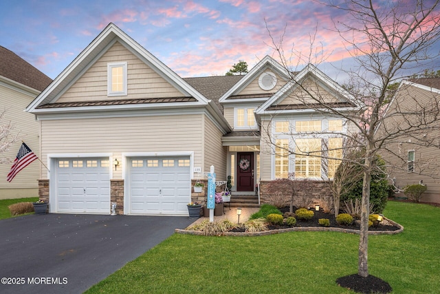 view of front of house featuring driveway, stone siding, a yard, metal roof, and a standing seam roof