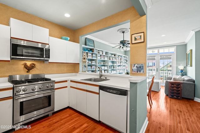 kitchen with stainless steel appliances, a sink, light countertops, white cabinetry, and light wood finished floors