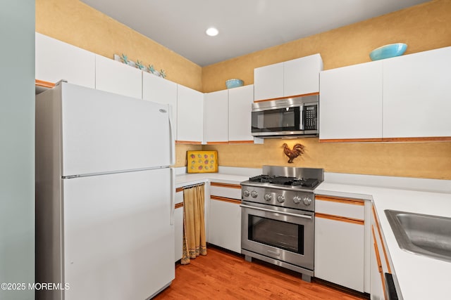 kitchen featuring appliances with stainless steel finishes, light countertops, white cabinets, light wood-type flooring, and a sink