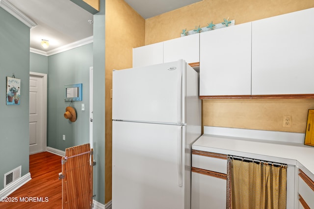 kitchen featuring freestanding refrigerator, wood finished floors, light countertops, white cabinetry, and ornamental molding