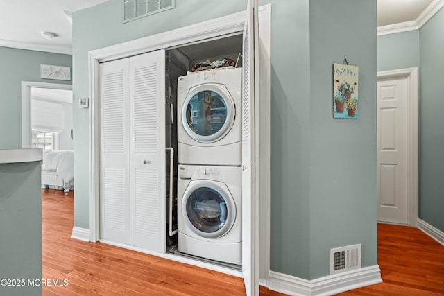 washroom with estacked washer and dryer, crown molding, wood finished floors, and baseboards