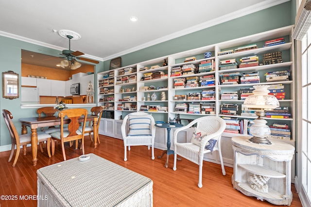 living area featuring ornamental molding, ceiling fan, wood finished floors, and baseboards