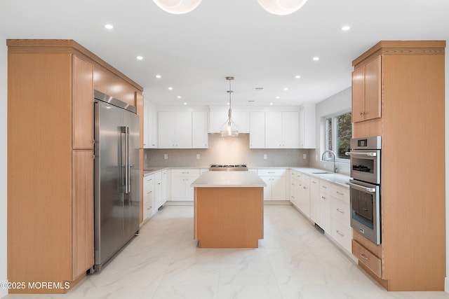 kitchen with a sink, marble finish floor, stainless steel appliances, light countertops, and a kitchen island