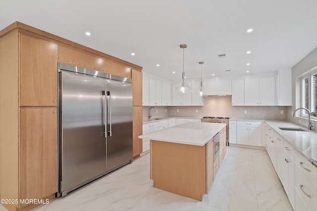 kitchen with a kitchen island, marble finish floor, built in appliances, and a sink