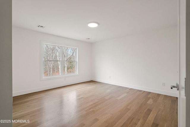 empty room featuring light wood finished floors, baseboards, and visible vents