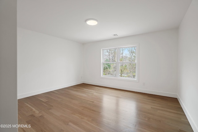 spare room featuring wood finished floors, visible vents, and baseboards