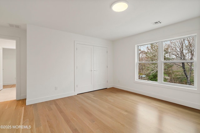 unfurnished bedroom with a closet, light wood-type flooring, visible vents, and baseboards