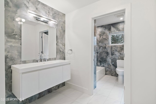 bathroom with vanity, tile walls, marble finish floor, a tub, and toilet