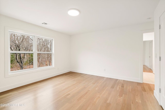 spare room with baseboards, light wood-style floors, and visible vents