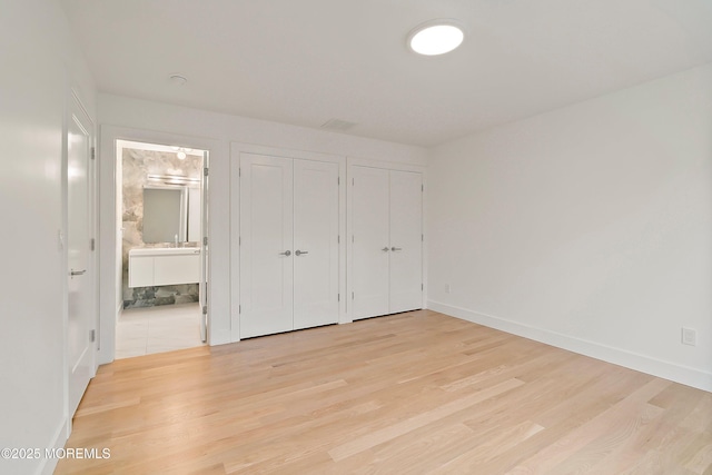 unfurnished bedroom with light wood finished floors, multiple closets, baseboards, and ensuite bathroom