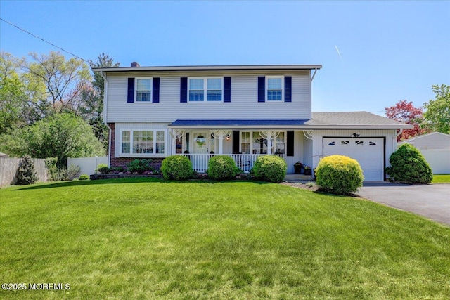 colonial home featuring fence, covered porch, a front yard, an attached garage, and driveway