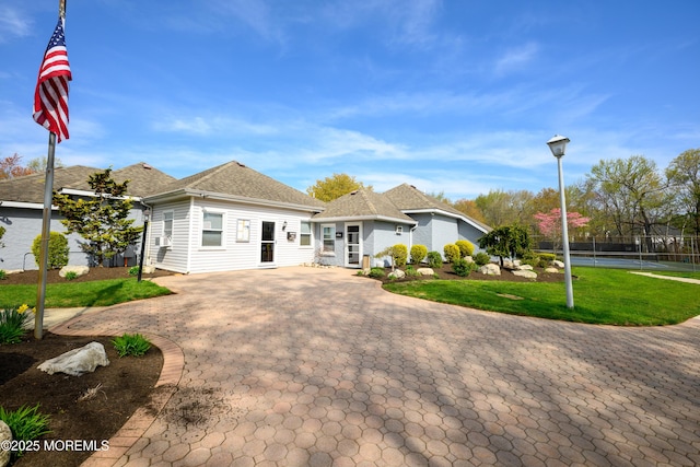 ranch-style home with curved driveway, fence, a front yard, and a tennis court