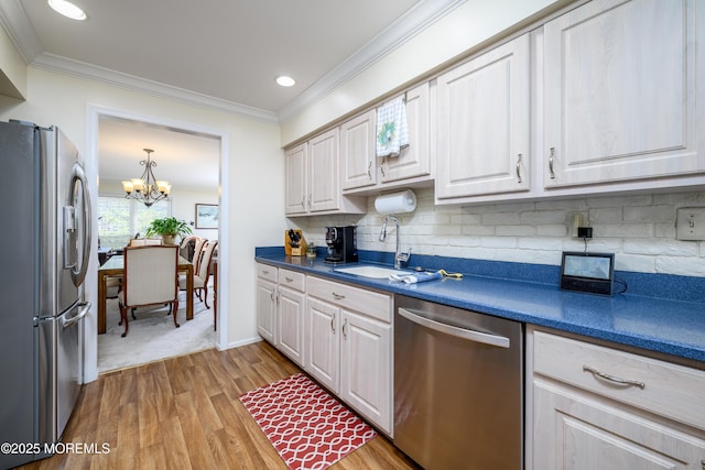 kitchen featuring crown molding, appliances with stainless steel finishes, dark countertops, a sink, and light wood-style flooring