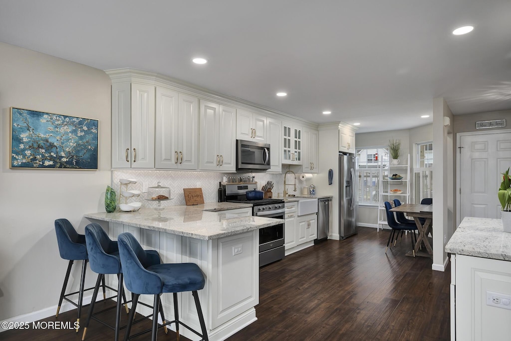kitchen featuring stainless steel appliances, a kitchen breakfast bar, dark wood-style flooring, backsplash, and white cabinetry