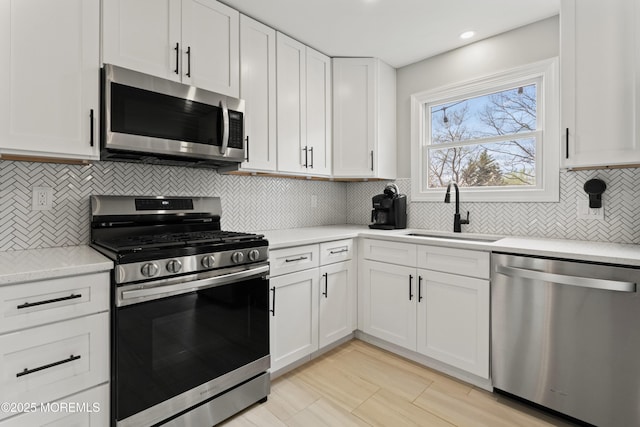 kitchen featuring tasteful backsplash, appliances with stainless steel finishes, light countertops, white cabinets, and a sink