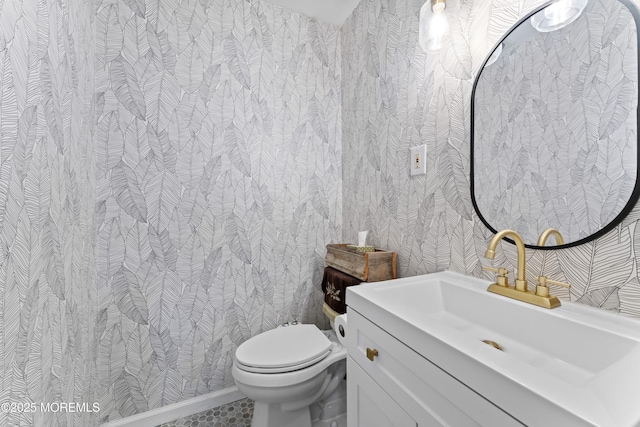 half bath featuring toilet, wallpapered walls, vanity, and baseboards