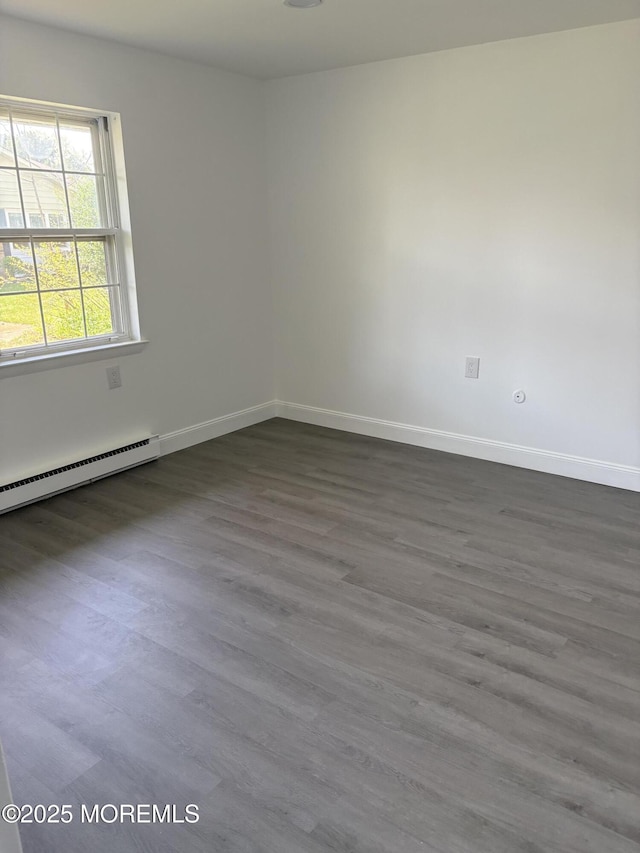 unfurnished room with dark wood-style flooring, a baseboard heating unit, and baseboards