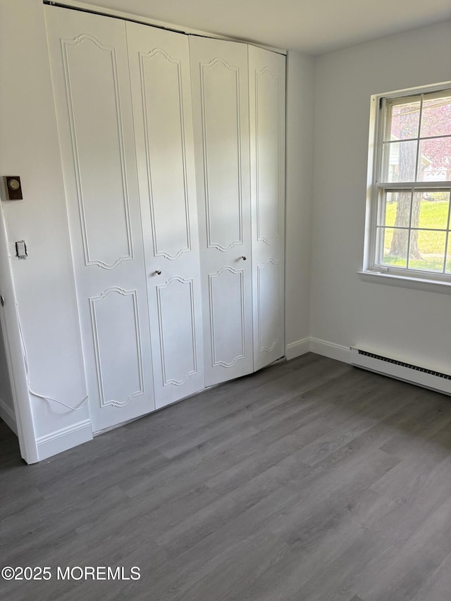 unfurnished bedroom with a closet, a baseboard radiator, wood finished floors, and baseboards