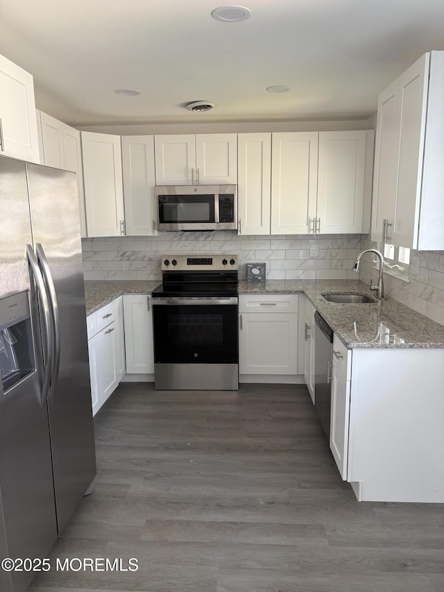 kitchen featuring light stone countertops, a sink, stainless steel appliances, decorative backsplash, and white cabinetry