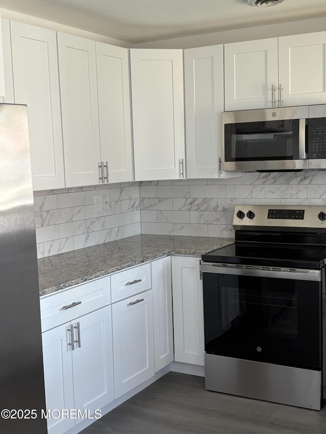kitchen with appliances with stainless steel finishes, light stone countertops, white cabinets, and dark wood-style floors