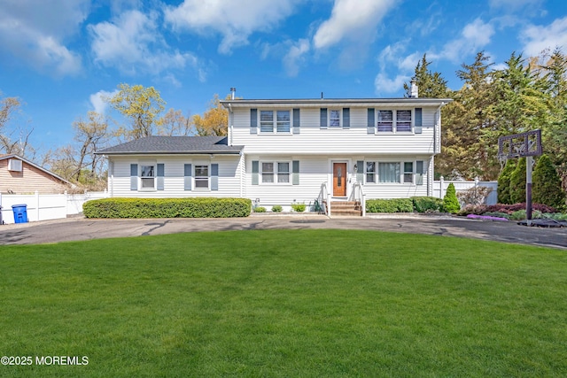colonial home featuring a front lawn, driveway, entry steps, and fence