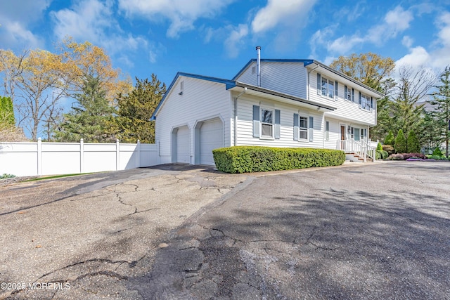 view of side of home with a garage, aphalt driveway, and fence