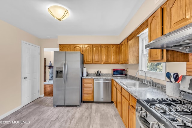 kitchen featuring brown cabinets, a sink, light wood-style floors, stainless steel appliances, and under cabinet range hood
