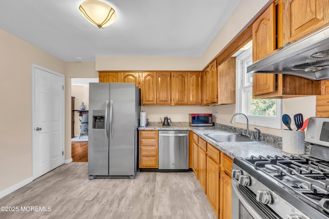 kitchen featuring under cabinet range hood, appliances with stainless steel finishes, brown cabinets, light wood finished floors, and a sink