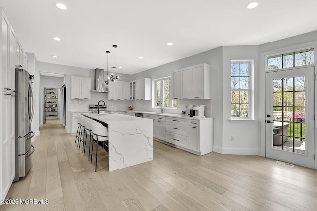kitchen with a kitchen breakfast bar, visible vents, a center island with sink, light wood-type flooring, and wall chimney exhaust hood