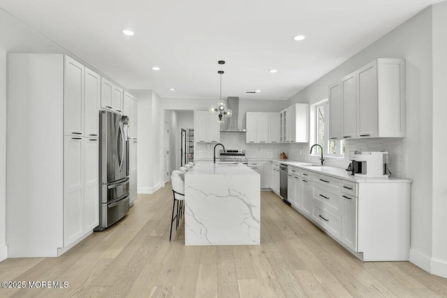 kitchen featuring light stone countertops, a sink, light wood-style floors, stainless steel appliances, and wall chimney exhaust hood