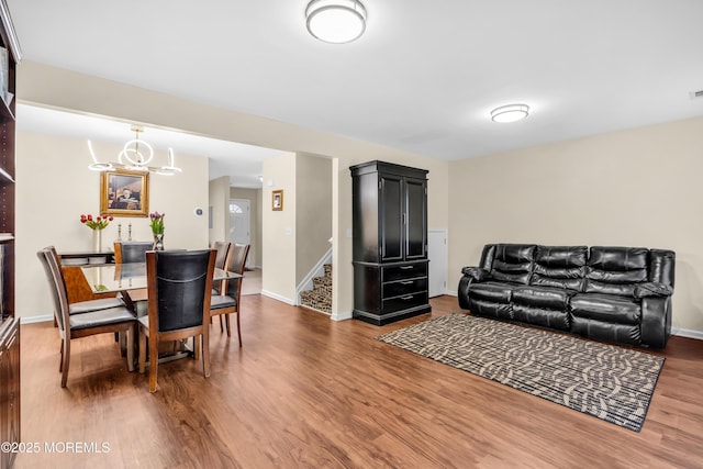 living room featuring an inviting chandelier, stairway, visible vents, baseboards, and wood finished floors