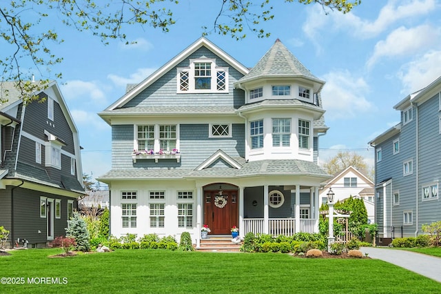 victorian house with a porch, roof with shingles, and a front yard