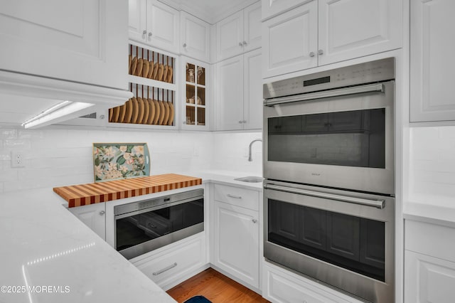 kitchen featuring white cabinetry, stainless steel double oven, and decorative backsplash