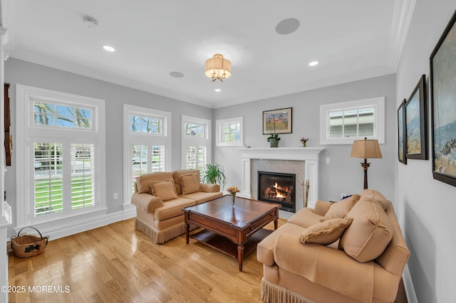 living room featuring recessed lighting, ornamental molding, light wood-style flooring, and a glass covered fireplace